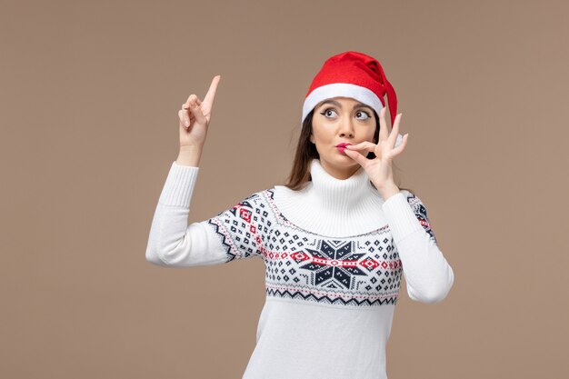 Вид спереди молодая женщина с красной рождественской шапкой на темно-коричневом фоне рождественские эмоции новый год