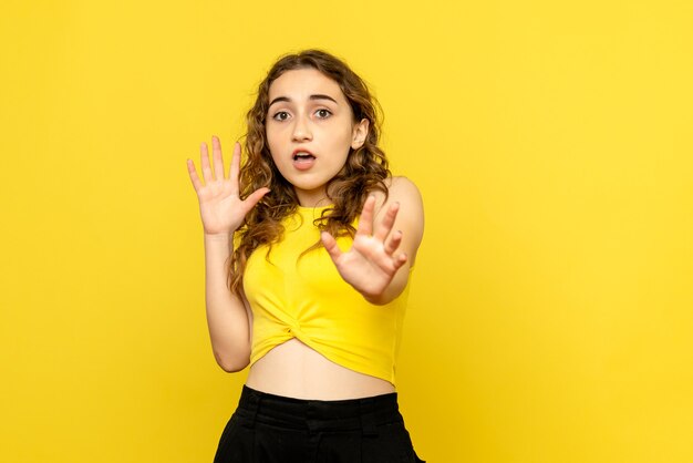 Front view of young woman with scared face on yellow wall