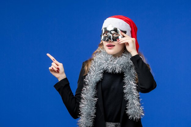 Front view of young woman with silver mask on blue wall