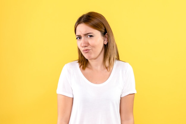 Front view of young woman with skeptical face on yellow wall