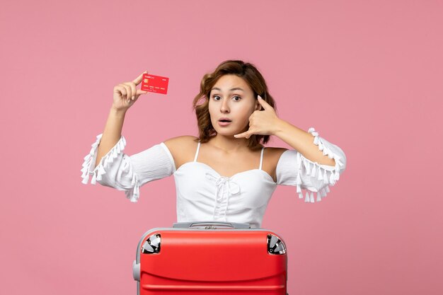 분홍색 벽에 은행 카드를 들고 휴가 가방을 들고 있는 젊은 여성의 전면 모습
