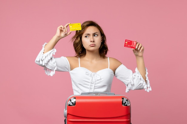 Vista frontale della giovane donna con la borsa delle vacanze che tiene le carte bancarie sulla parete rosa