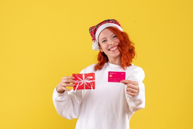 クリスマスプレゼントと黄色の壁に銀行カードを持つ若い女性の正面図