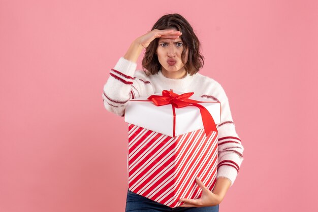 Front view of young woman with xmas present on pink wall