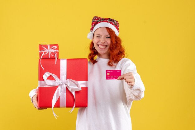 Front view of young woman with xmas presents and bank card on yellow wall