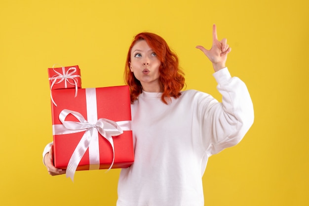 Front view of young woman with xmas presents on yellow wall