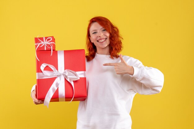 Вид спереди молодой женщины с рождественскими подарками на желтой стене