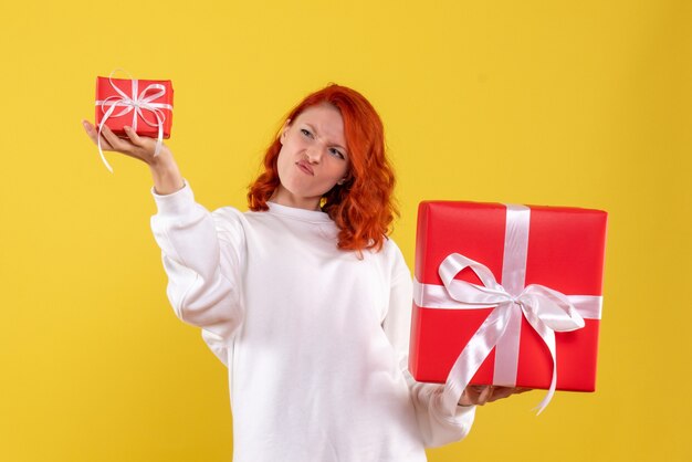 Front view of young woman with xmas presents on yellow wall
