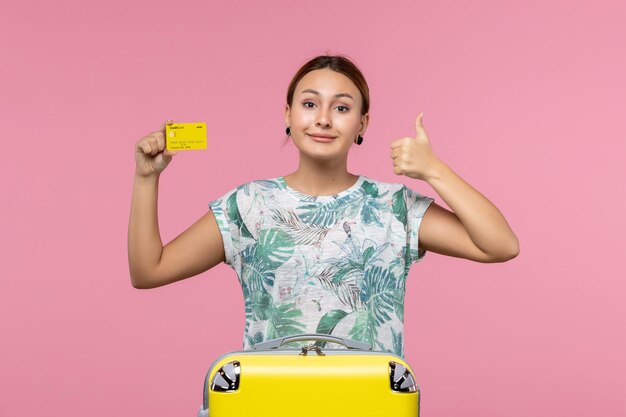 분홍색 벽에 노란색 은행 카드와 가방을 든 젊은 여성의 전면