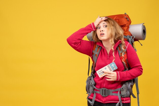 Front view of young worried and emotional travelling girl in medical mask holding ticket