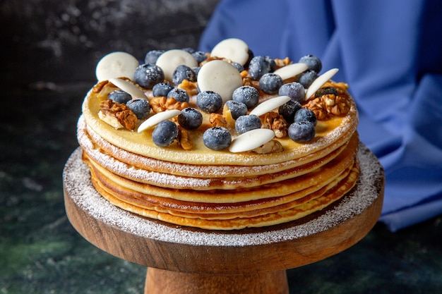 Front view yummy cake with walnuts blueberries and cookies dark surface