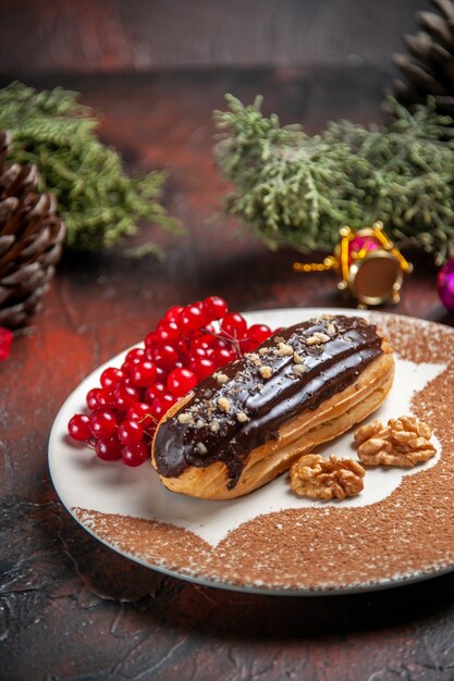 Вид спереди вкусные шоколадные эклеры с красными ягодами на темном столе торт пирог десерт сладкий