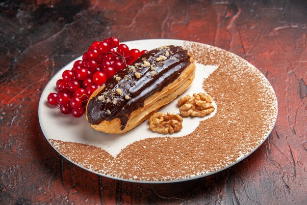 Вид спереди вкусные шоколадные эклеры с красными ягодами на темном столе пирог десертный торт сладкий