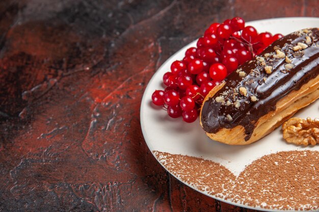 Front view yummy choco eclairs with red berries on dark table, pie dessert cake sweet