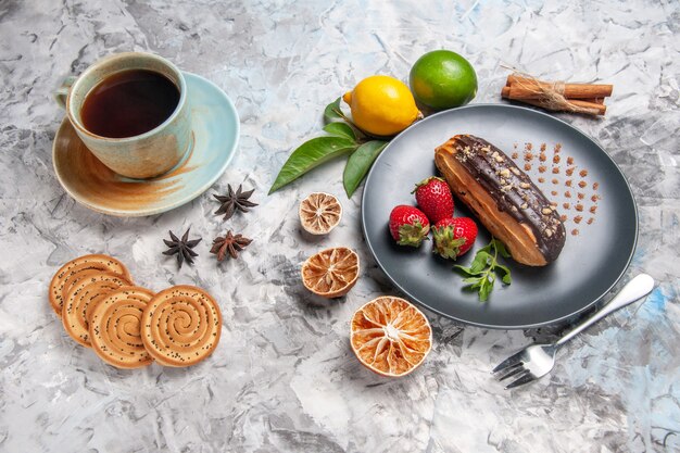 ライトテーブルのデザートケーキビスケットにお茶とフルーツを添えた正面図のおいしいチョコエクレア