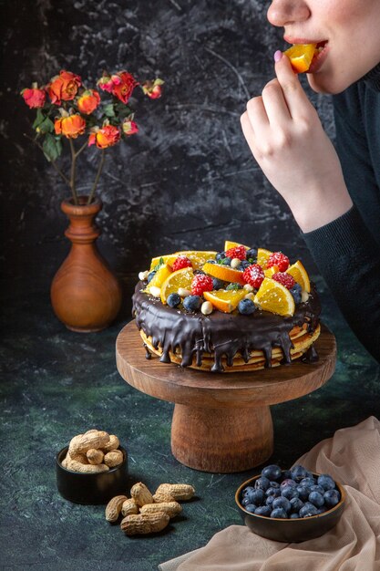 暗い壁に女性が新鮮な果物で飾られている正面のおいしいチョコレートケーキ