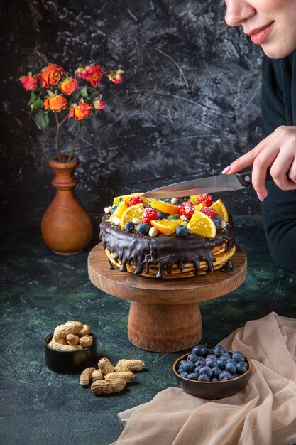 暗い壁に女性によってカットされている果物と正面図おいしいチョコレートケーキ