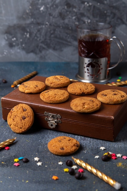 Front view yummy chocolate cookies on the brown case with colored little star signs and candles on the dark-grey background cookie sweet tea