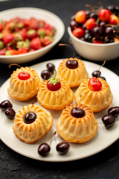 A front view yummy cookies inside white plate with cherries strawberries on the dark desk fruit biscuit cake 