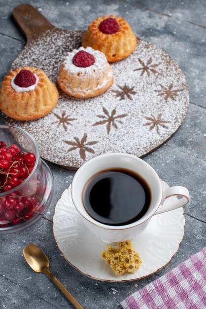 一杯のコーヒーと灰色の机の甘いフルーツに新鮮な赤いクランベリーと正面のおいしいdケーキ