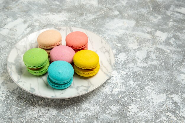 Vista frontale yummy macarons francesi torte colorate all'interno della piastra sulla superficie bianca torta zucchero biscotto torta dolce biscotto