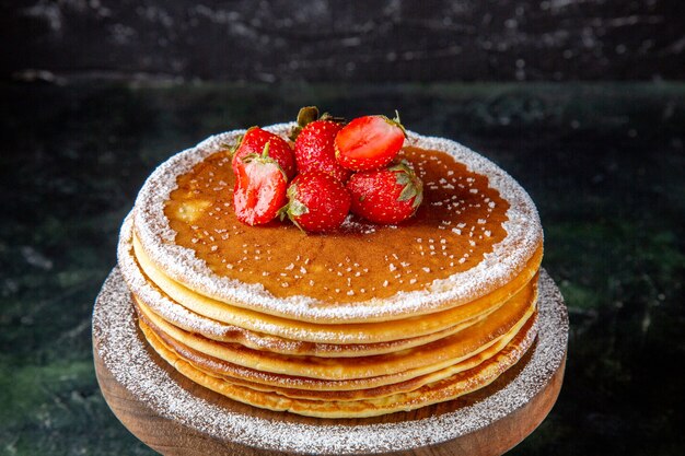 Front view yummy honey cake with fresh strawberries on round wooden board dark surface