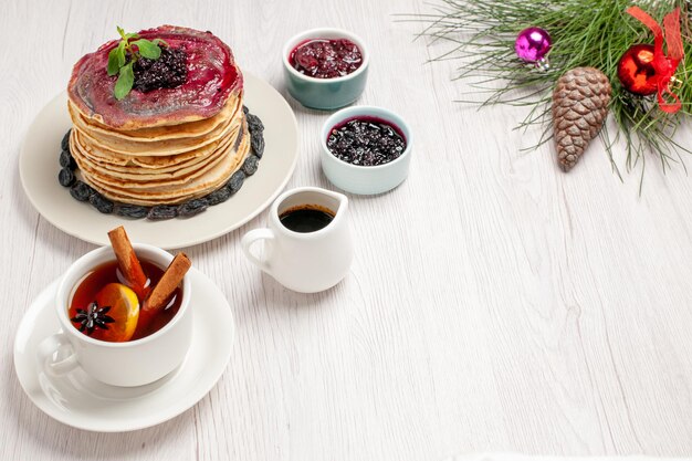 Front view yummy jelly pancakes with raisins and cup of tea on white space