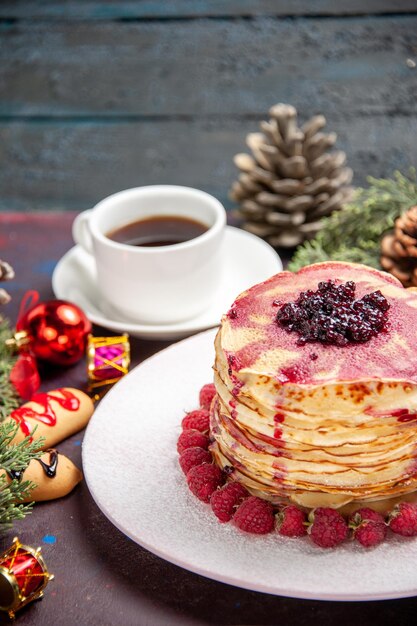 Front view yummy jelly pancakes with strawberries and cup of tea on dark space