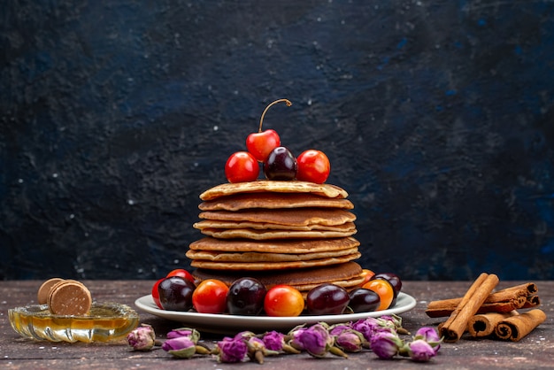 A front view yummy pancakes with cherries inside white plate with cinnamon on the dark desk fruit pancake