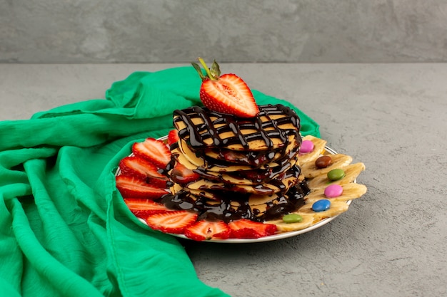 Foto gratuita frittelle gustose vista frontale con fragole rosse a fette di cioccolato e banane all'interno del piatto bianco sul pavimento grigio