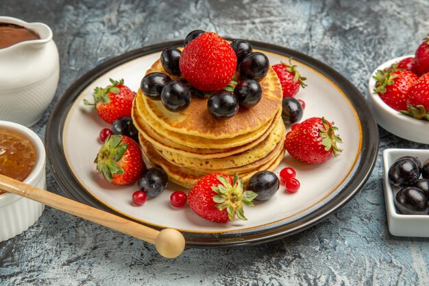 Front view yummy pancakes with fresh fruits and honey on light surface fruit cake sweet