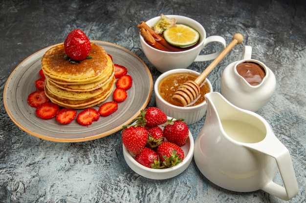 Front view yummy pancakes with fruits and cup of tea on light surface sweet cake fruit