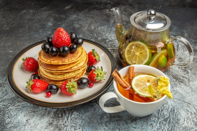 Front view yummy pancakes with fruits and tea on light surface fruit sweet breakfast