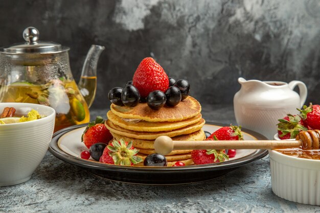 Front view yummy pancakes with fruits and tea on light surface sweet fruit breakfast