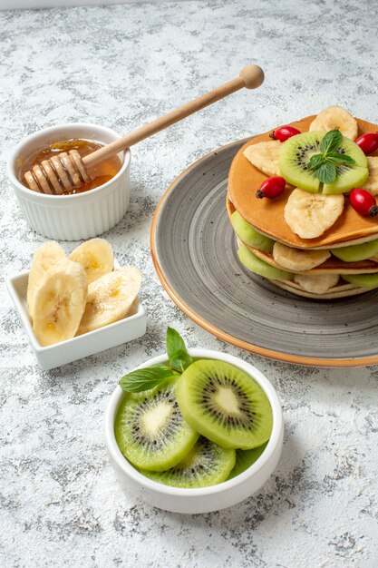 Front view yummy pancakes with honey and sliced fruits on the white surface