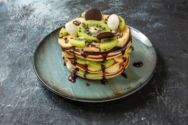 Front view yummy pancakes with sliced fruits and chocolate on dark-grey surface