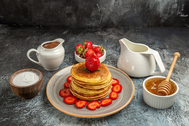 Front view yummy pancakes with strawberries and honey on light surface fruit cake sweet