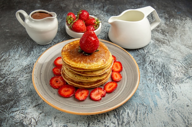 Front view yummy pancakes with strawberries and honey on light surface sweet fruit cake