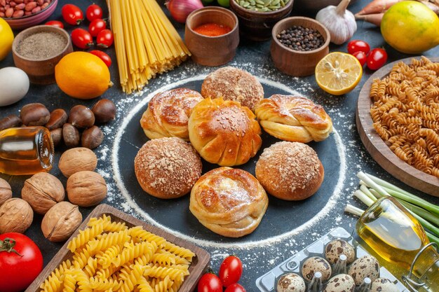 Front view yummy sweet buns around vegetables pasta nuts and seasonings on dark background photo color meal health diet raw pastry