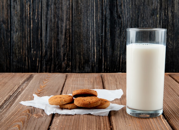 Front viewoatmeal cookies on tracing paper with glass of milk on a wooden background