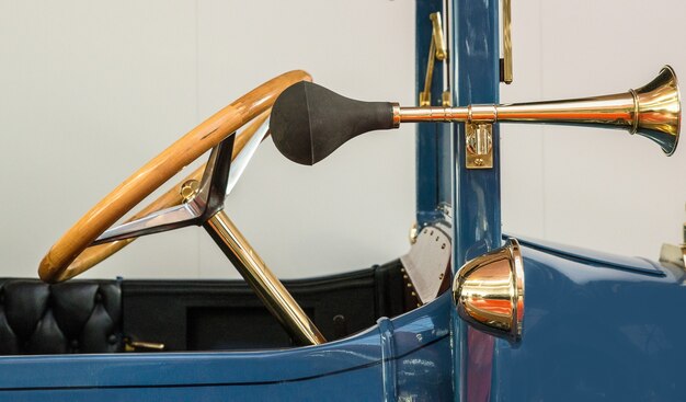 Front of a vintage blue car with an antique golden steering wheel and a separate horn