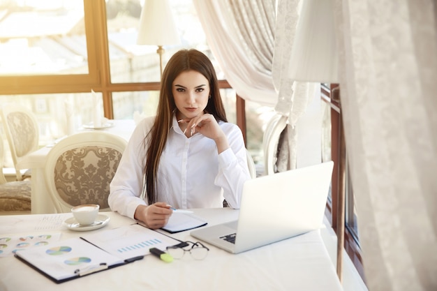 Frontview of a working place with a young beautiful brunette woman who is looking straight, surrounded with lots of diagrammes