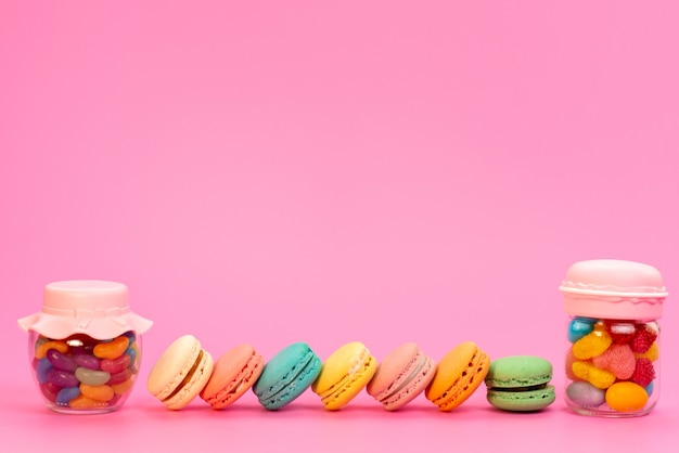 A frotn view french macarons along with multicolored candies inside cans on pink