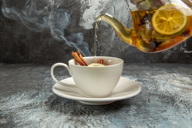 Frotn view kettle with tea pouring into cup on dark surface tea ceremony morning