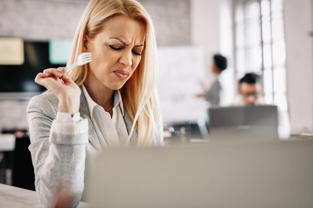 Frowning businesswoman doesn't like taste of food she is eating on lunch break