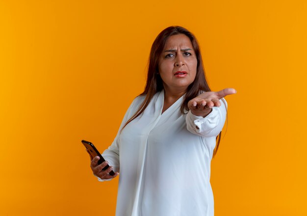 Frowning casual caucasian middle-aged woman holding phone and holding out hand