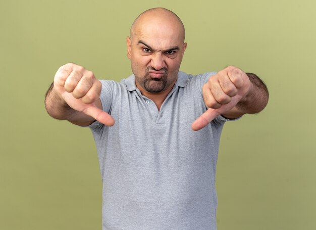 Frowning casual middle-aged man showing thumbs down isolated on olive green wall