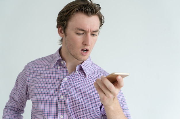 Frowning concentrated man recording voice message while using smartphone.