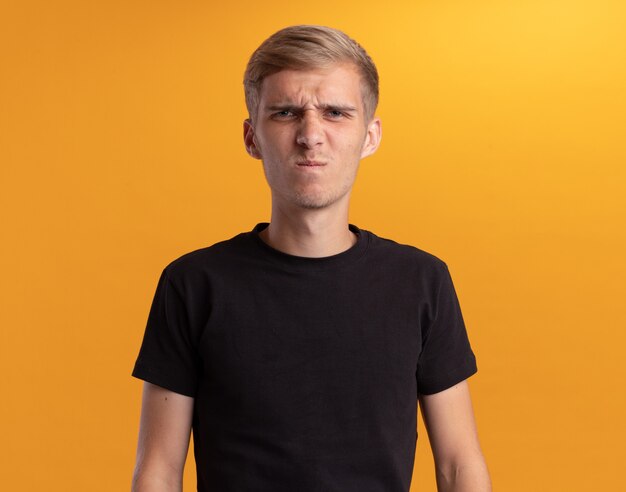 Frowning looking at front young handsome guy wearing black shirt isolated on yellow wall