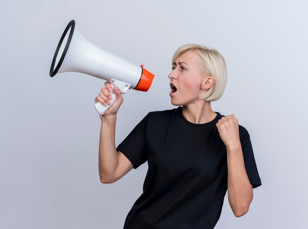 Frowning middle-aged blonde woman looking at side talking by speaker clenching fist isolated on white wall